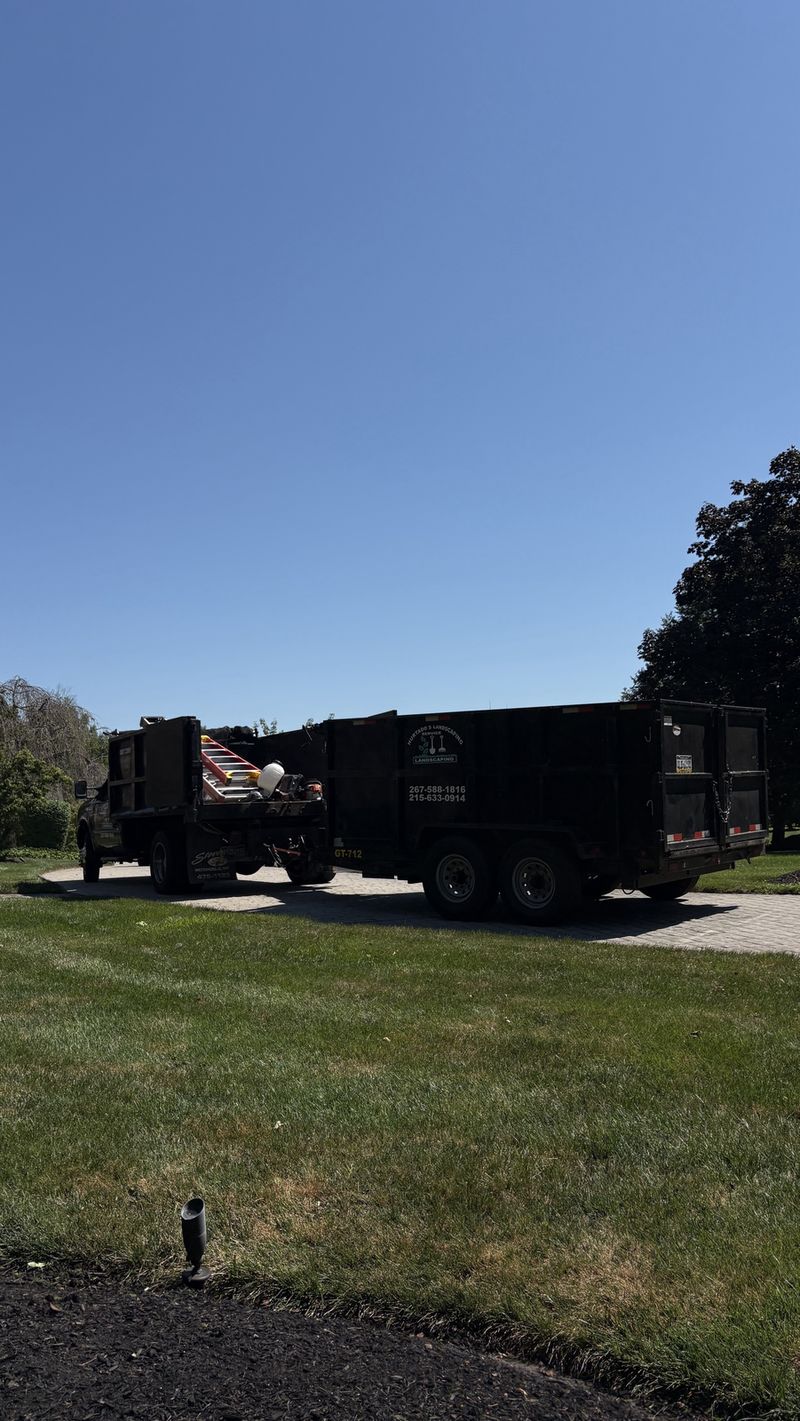 Hurtado's dump truck and dump trailer with the company logo, parked on a paver driveway